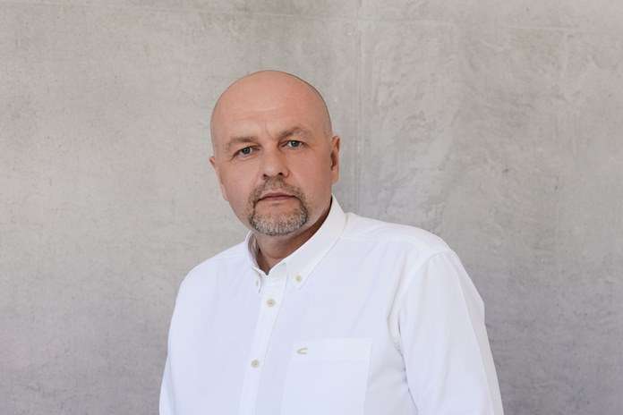 Linas Ivanauskas baltais marškiniais prieš pilką sieną.