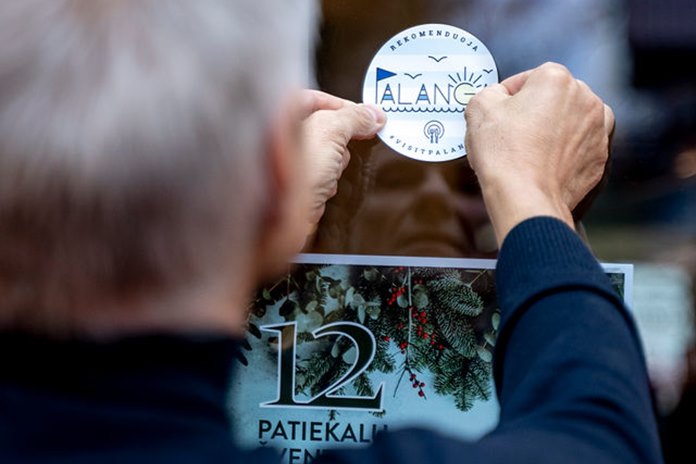 Asmuo klijuoja kokybės ženklą „Palanga rekomenduoja“ ant maitinimo įstaigos durų.